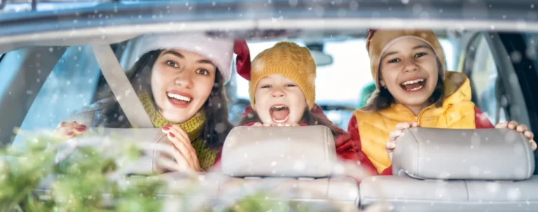 Due bambine e una ragazza con cappello di babbo Natale sorridono in un’auto