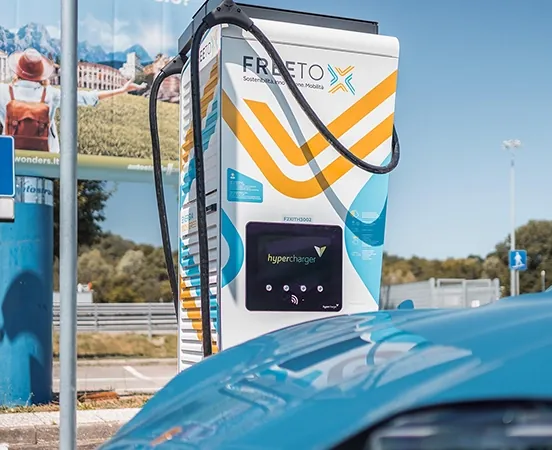 A Free To X charging station, in the background of a car with the same colors as the Free To X logo