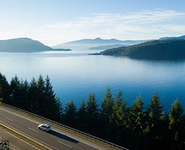 A car drives down a road with the breathtaking view of a lake in the background